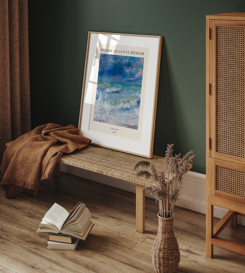 May include: A framed print of a painting by Pierre-Auguste Renoir titled "Seascape" from 1887. The print is hanging on a green wall above a wooden bench with a brown blanket draped over it. A wicker vase with dried flowers sits on the floor next to the bench.