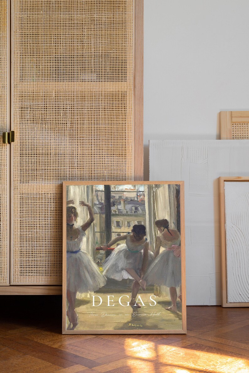 May include: A framed print of a painting by Edgar Degas titled "Three Dancers in an Opera Hall". The painting depicts three ballerinas in white tutus, practicing in a room with a window overlooking a city.
