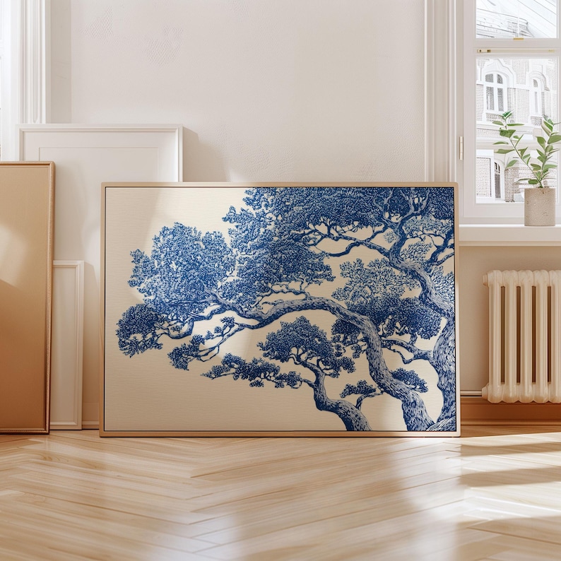 May include: A framed art print with a blue and white tree illustration. The artwork has a beige background and is in a light brown wooden frame. The print is displayed in a room with a window and wooden flooring.