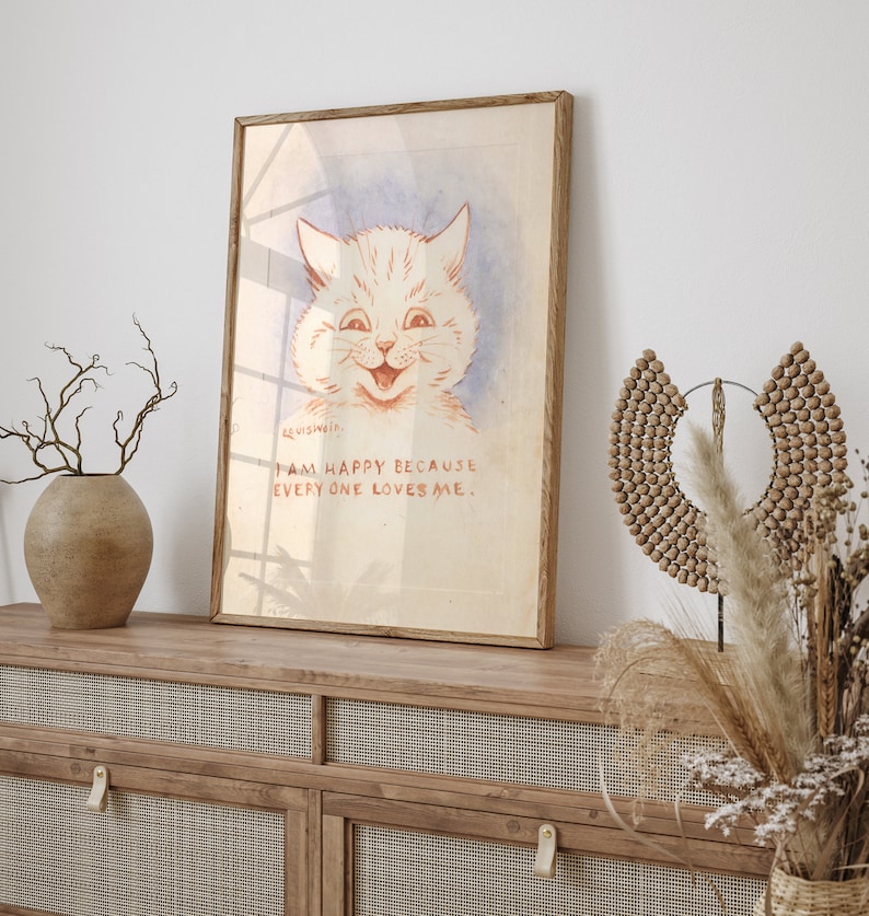 May include: A framed print of a white cat with a big smile. The cat is drawn in a vintage style with red and pink tones. The text below the cat reads "I am happy because everyone loves me."
