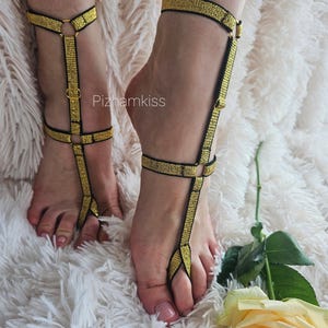 May include: A pair of gold and black elastic foot jewelry pieces featuring a toe loop, an ankle strap, and a vertical connector strap with metal rings and sliders. The text Pizhamkiss is visible in the center of the image.