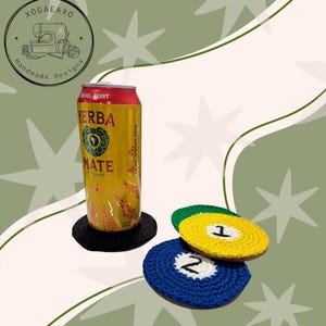 May include: A crochet PDF pattern image featuring a can of Yerba Mate on a black coaster, with three colorful crochet coasters shaped like billiard balls. The coasters are blue, yellow, and green, with the numbers 1 and 2 on them. The background is a light green color.