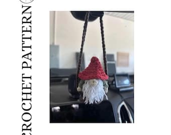 Op de afbeelding: Een gehaakte kabouter auto-hanger met een rode hoed, witte baard en groen en bruin lichaam. De kabouter hangt aan een bruin koord. De tekst "CROCHET PATTERN" staat verticaal afgedrukt.