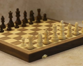 May include: A wooden chessboard with a walnut finish and a light-colored wood playing surface. The board is set up for a game of chess with black and white pieces in place.
