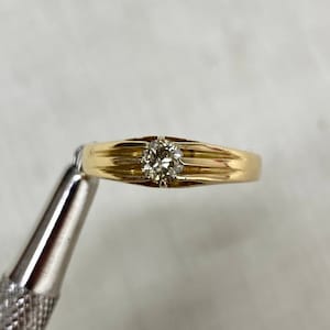 Op de afbeelding: Een gouden ring met een enkele ronde diamant in het midden.