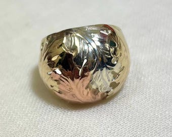 May include: A gold-toned ring with a floral design. The ring has a rounded shape and features intricate carvings of leaves and flowers. The metal has a mix of gold and rose gold tones, creating a unique and elegant look.