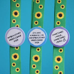 Könnte beinhalten: Drei runde Buttons mit Text auf grünen Bändern mit Sonnenblumenmuster. Die Buttons tragen die Aufschriften: "AMBULATORY WHEELCHAIR USER", "IT'S NOT A MIRACLE, I'M AN AMBULATORY WHEELCHAIR USER" und "SOMETIMES I WALK, SOMETIMES I ROLL &."