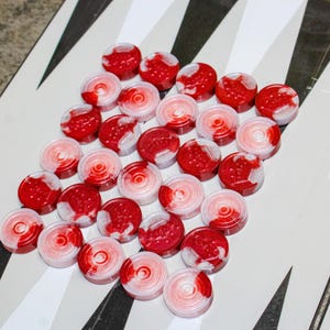 May include: A collection of red and white game chips arranged in a triangular pattern on a black and white checkerboard.