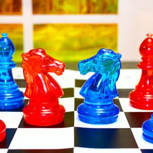 Peut inclure: Gros plan sur un échiquier avec des pièces d'échecs translucides rouges et bleues. Les pièces comprennent des pions, des fous et des cavaliers. Les cavaliers se font face. L'échiquier est noir et blanc.