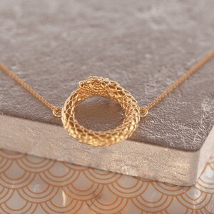 May include: A gold snake necklace with a snake head forming a circle. The snake is detailed with scales and has a smooth, shiny finish.