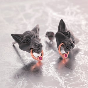May include: A pair of silver wolf head stud earrings with rose gold rings and pink gemstones.