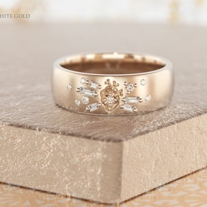 May include: A white gold band ring with a heart design and small diamonds. The ring is on a textured surface.