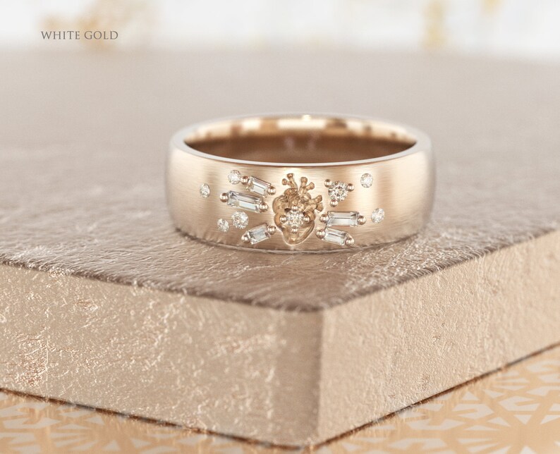 May include: A white gold band ring with a heart design and small diamonds. The ring is on a textured surface.