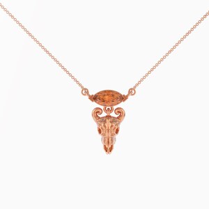 May include: A rose gold necklace with a small, detailed skull pendant and a brown gemstone. The chain is a delicate, linked style.