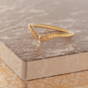 May include: A gold ring with a snake-like design and a single diamond accent. The ring is on a textured surface.