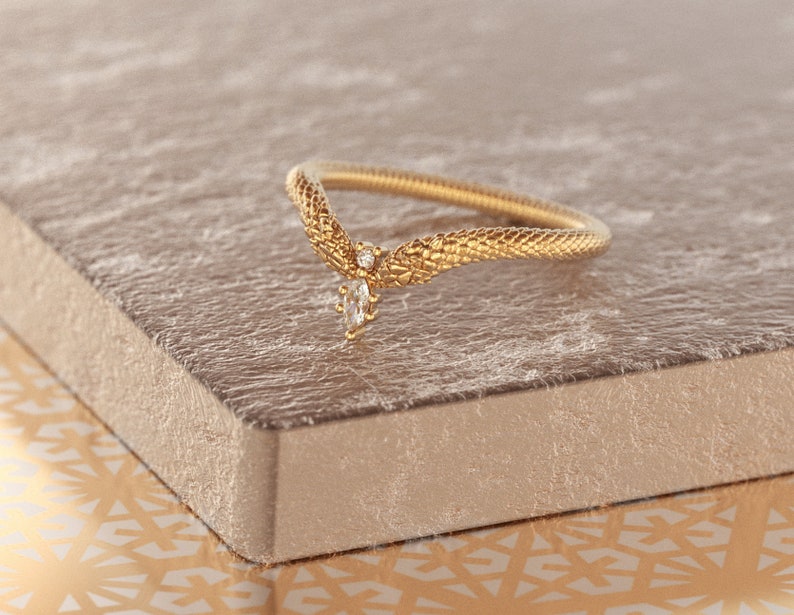 May include: A gold ring with a snake-like design and a single diamond accent. The ring is on a textured surface.