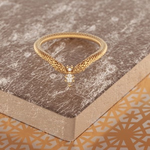 May include: A gold ring with a delicate, textured design resembling a snake. A single diamond is set in the center of the ring.