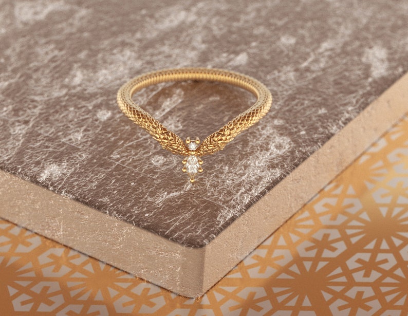 May include: A gold ring with a delicate, textured design resembling a snake. A single diamond is set in the center of the ring.