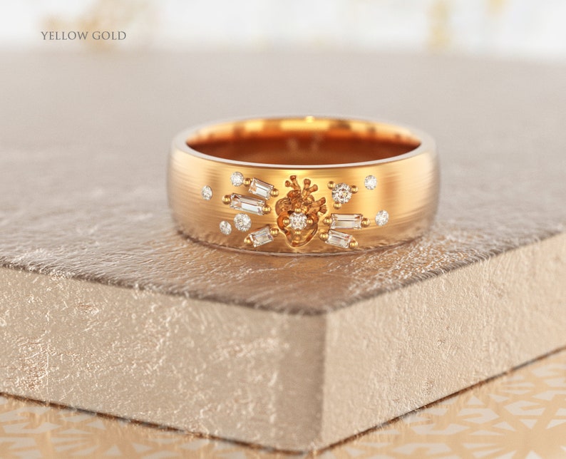 May include: A gold band ring with a heart-shaped design and small diamonds set around it. The ring is made of yellow gold and has a brushed finish.