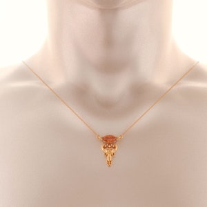 May include: A gold chain necklace with a pendant featuring a small, orange gemstone and intricate gold detailing.