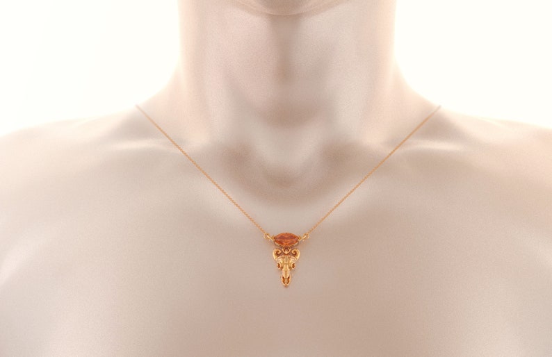 May include: A gold chain necklace with a pendant featuring a small, orange gemstone and intricate gold detailing.