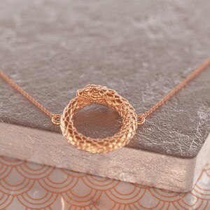 May include: A gold snake necklace with a circular pendant. The snake is coiled into a circle with its head facing the viewer.
