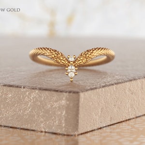 May include: A delicate gold ring with a textured band and a small diamond cluster in the center. The ring is set on a light brown surface. "YELLOW GOLD" is written in the top left corner of the image.