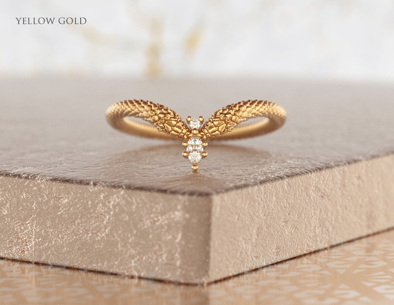 May include: A delicate gold ring with a textured band and a small diamond cluster in the center. The ring is set on a light brown surface. "YELLOW GOLD" is written in the top left corner of the image.