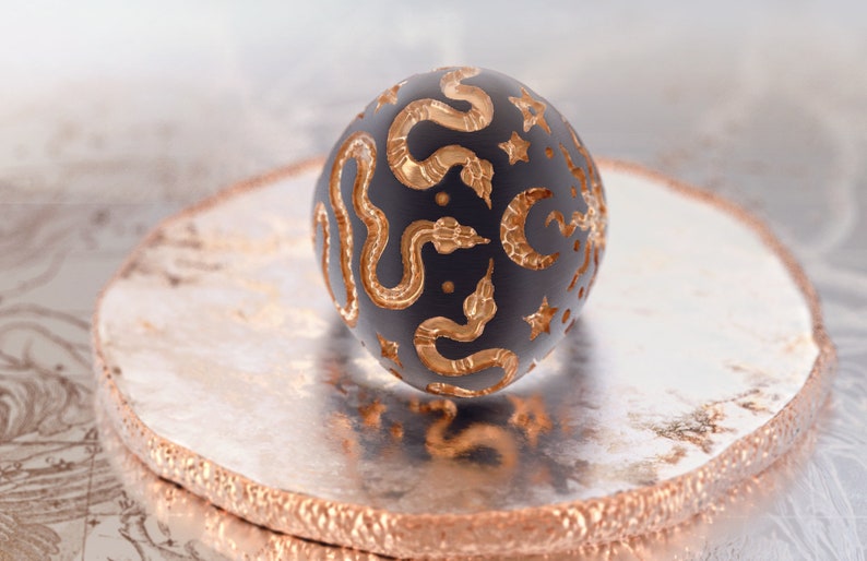 May include: A black sphere with a gold snake and star pattern. The sphere is sitting on a silver and gold circular stand.