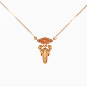 May include: A gold necklace with a detailed skull pendant and a small, orange gemstone.