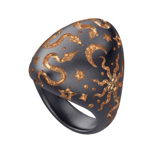 May include: A black ring with a gold design of snakes, stars, and moons. The ring is made of metal and has a smooth, polished finish.