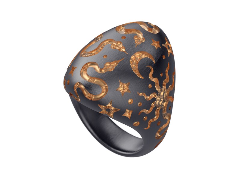 May include: A black ring with a gold design of snakes, stars, and moons. The ring is made of metal and has a smooth, polished finish.