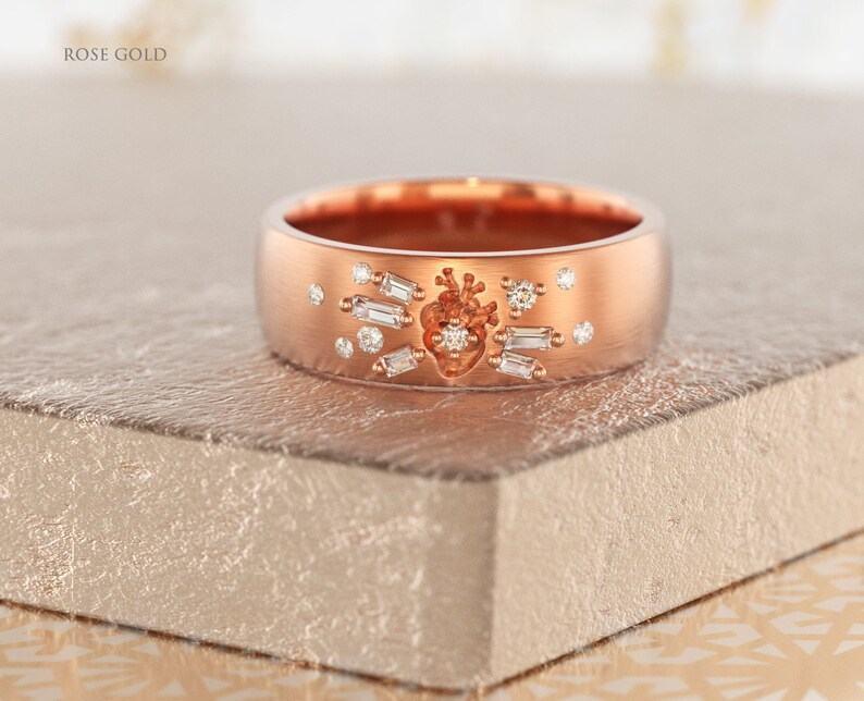 May include: A rose gold band ring with a heart design and small diamonds. The ring is on a textured surface.