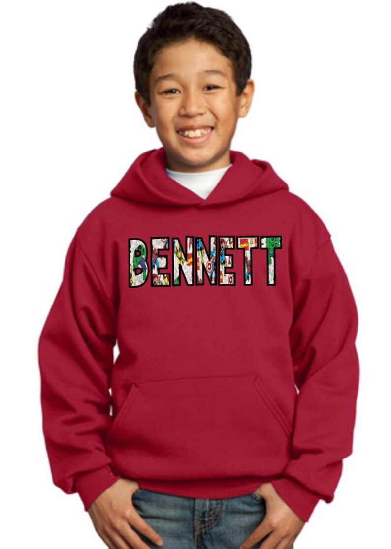 May include: Red hooded sweatshirt with a pocket on the front. The name "BENNETT" is printed on the front in black with a colorful comic book design.