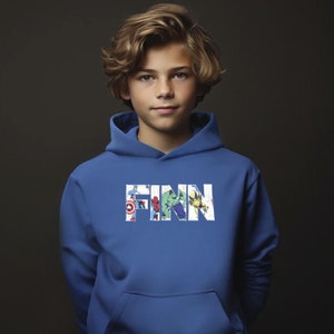May include: A blue hooded sweatshirt with the name "FINN" printed in white letters. The letters are filled with images of various superheroes, including Spiderman, Hulk, and Captain America.