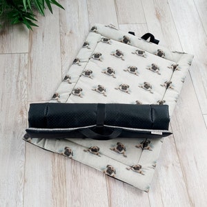 May include: A black and white dog bed with a pattern of pugs. The bed is rolled up and has a black strap.