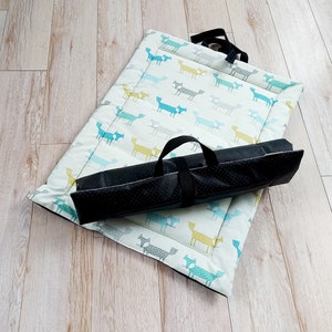 May include: A white and blue pet bed with a black carrying case. The bed features a repeating pattern of foxes in blue, yellow, and grey.
