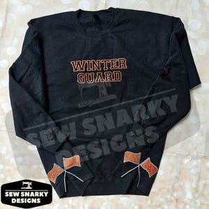 May include: Black sweatshirt with the text "WINTER GUARD" in orange on the front. The sweatshirt has orange and white glitter designs on the cuffs.