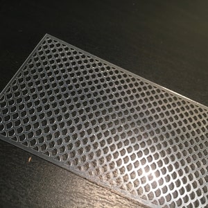 May include: A silver metal sheet with a repeating pattern of small, rounded shapes. The sheet is slightly curved and has a shiny finish.