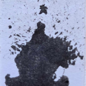 May include: A dark grey ink blot on a white background. The ink has a splatter effect and resembles a flame or a tree.