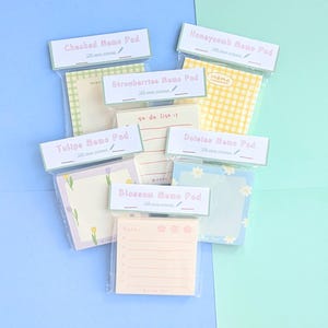 Puede incluir: Surtido de blocs de notas coloridos con varios diseños, incluyendo a cuadros, panal de abeja, fresas, tulipanes, margaritas y flores. Cada bloc tiene un título y el texto "100 hojas incluidas".