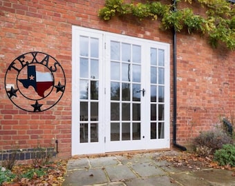 May include: A black metal Texas state outline with the word "TEXAS" in a circle around it. The state outline is filled with the colors of the Texas flag. The metal sign is mounted on a brick wall next to a white French door.