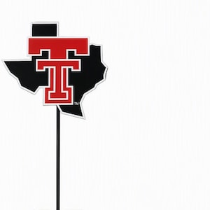 May include: A black metal yard sign featuring the silhouette of the state of Texas with a red and white Texas Tech University logo centered on the front. The sign is attached to a thin black metal stake with a two-pronged base for ground insertion.