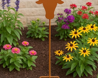May include: A rusty brown metal garden stake featuring the silhouette of a longhorn steer. The stake is planted in a flower bed with pink, yellow, purple, and red flowers. The background is a brick wall.