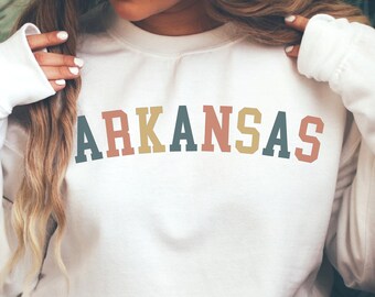 Può includere: Felpa bianca con la parola "ARKANSAS" stampata in lettere retrò colorate.