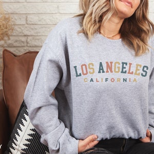 May include: A gray sweatshirt with the text "LOS ANGELES CALIFORNIA" in a rainbow arch design.