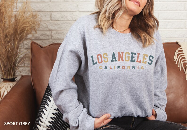 May include: A gray sweatshirt with the text "LOS ANGELES CALIFORNIA" in a rainbow arch design.