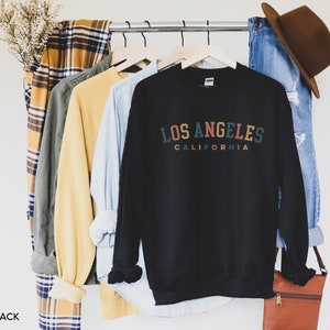 May include: Black sweatshirt with a vintage-style graphic that reads "Los Angeles, California" in colorful text.