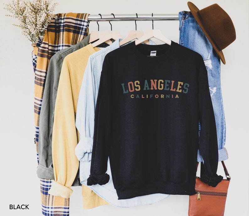 May include: Black sweatshirt with a vintage-style graphic that reads "Los Angeles, California" in colorful text.