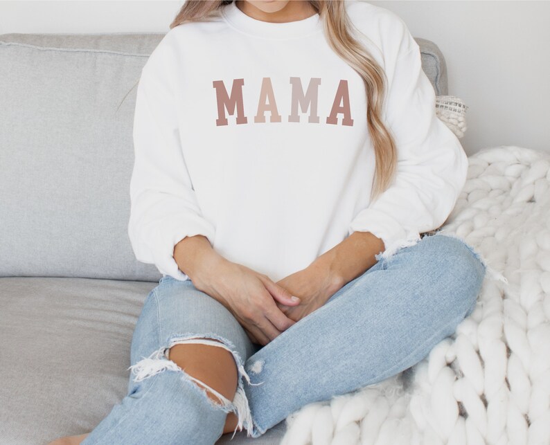 May include: White sweatshirt with a gradient pink and brown "MAMA" graphic.